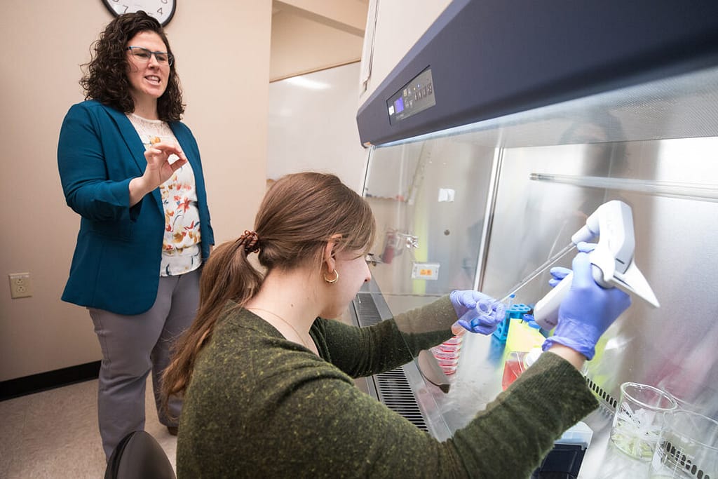 Assistant Professor Lyndsay Avery oversees a student in a lab working with a tissue culture.
